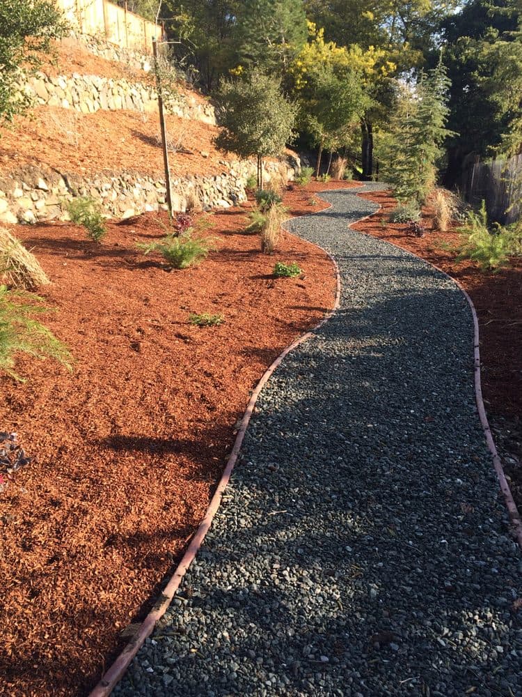 Curved gravel pathway winding up a mulched hillside above a natural stone retaining wall