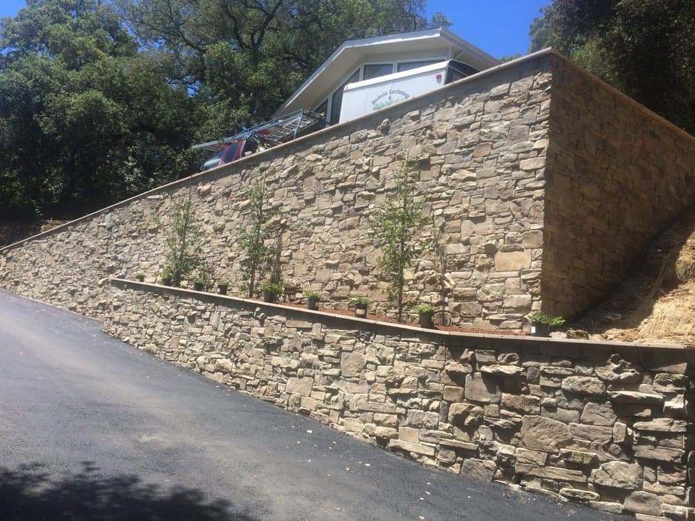 Tall natural stone retaining wall terracing a Bay Area hillside above a driveway