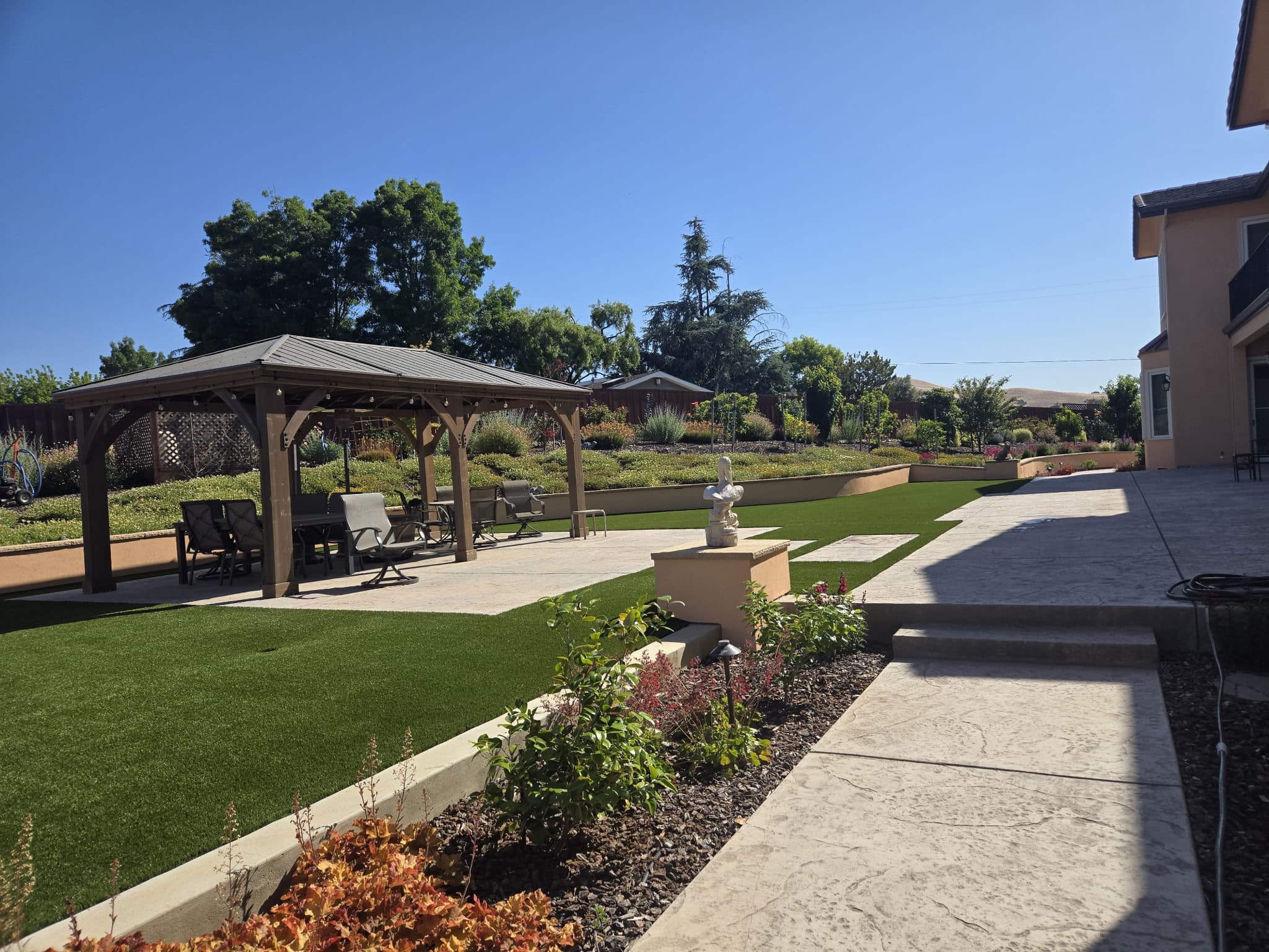 Fully landscaped Bay Area backyard with a cedar gazebo, manicured lawn, layered garden beds, and stamped concrete under a clear sky